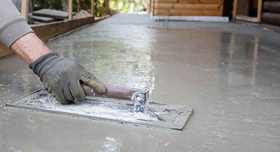 A person with gloves leveling cement using tool
